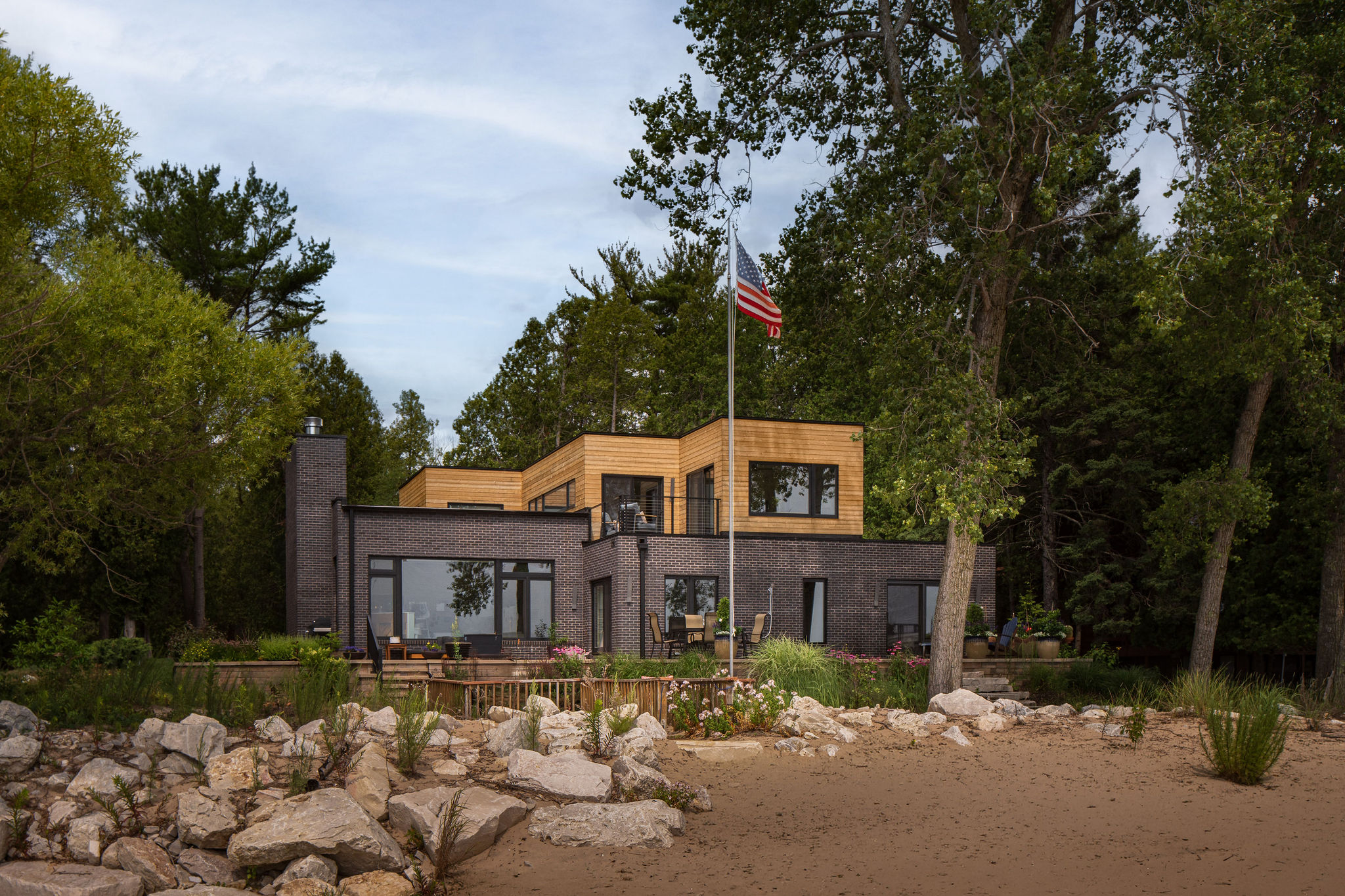 The MCM Lake House – Lake Michigan Exterior Lake Michigan side of a mid-century modern lake house with black brick, warm wood and expansive windows