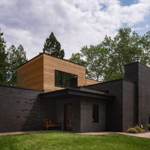 The MCM Lake House – Front Exterior Front exterior of a mid-century modern lake house with black brick and natural wood siding