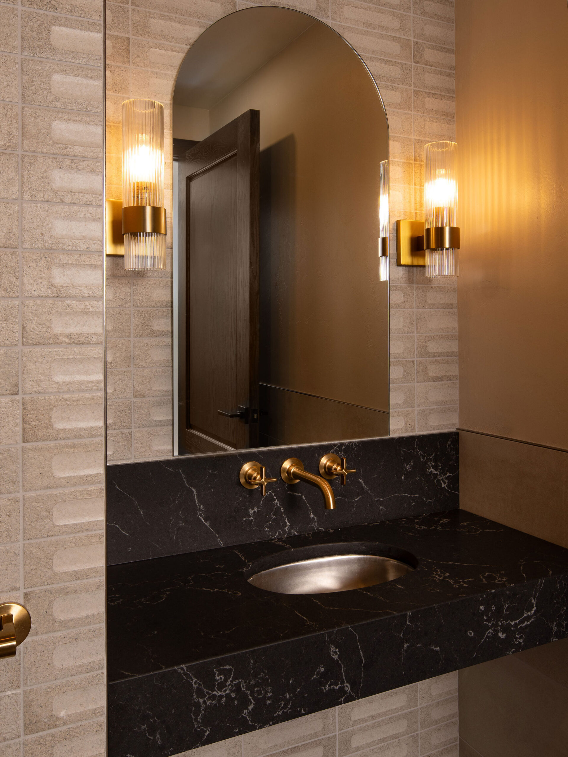 Restroom interior at The Blind Horse Terrace in Kohler, Wisconsin, with textured tile, black quartz, and brass fixtures