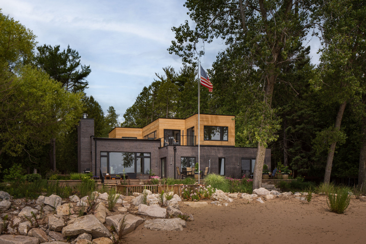 Lake Michigan side of a mid-century modern lake house with black brick, warm wood and expansive windows